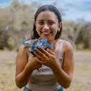 Portrait of a happy woman holding a bouquet of blue flowers, smiling joyfully outdoors.